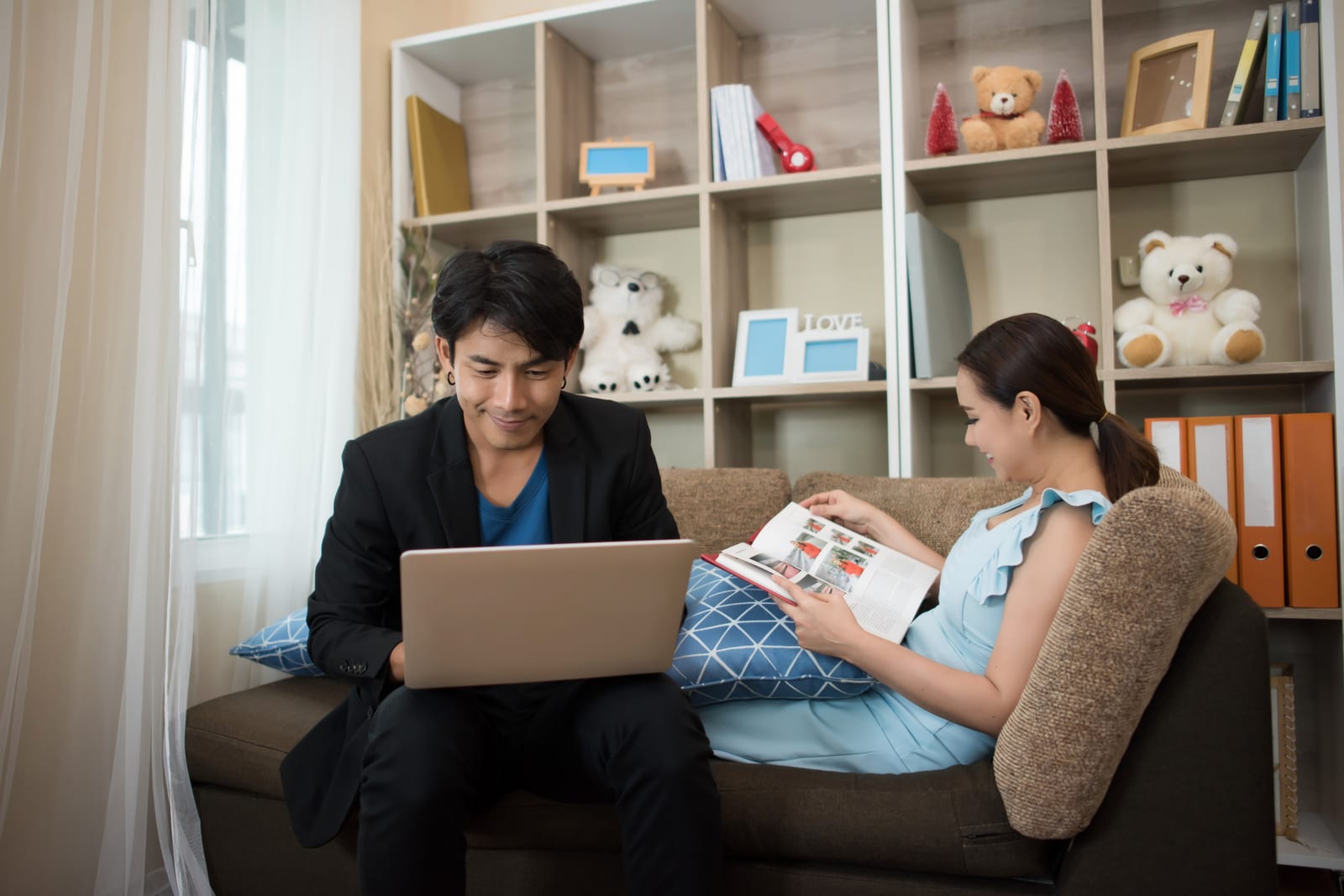 リビングのソファでくつろぎ、ノートパソコンと雑誌を手にする夫婦